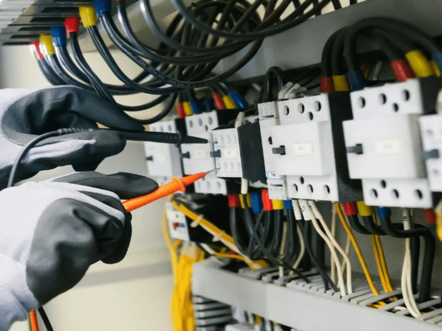 Gloved technician testing components inside an electrical control panel